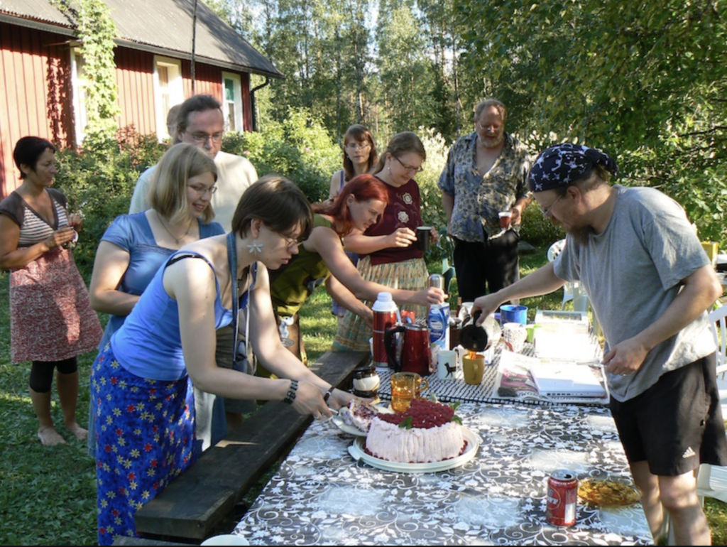 Usvan kesäleirillä 2013 ihmisiä on kokoontunut pihalle pöydän ympärille ottamaan täytekakkua.