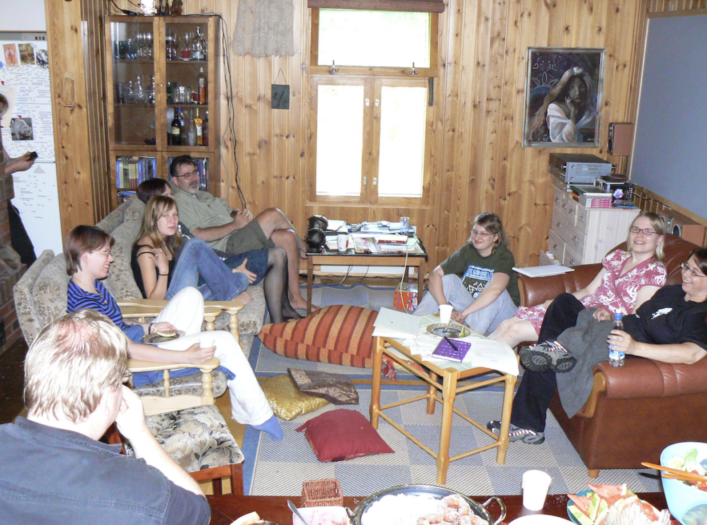 Usvan kesäleiri 2007: koolla joukko kirjoittajia olohuoneessa  sohvilla ja nojatuoleissa. Pienillä pöydillä on papereita, etualan pöydällä ruokatarjoilu.